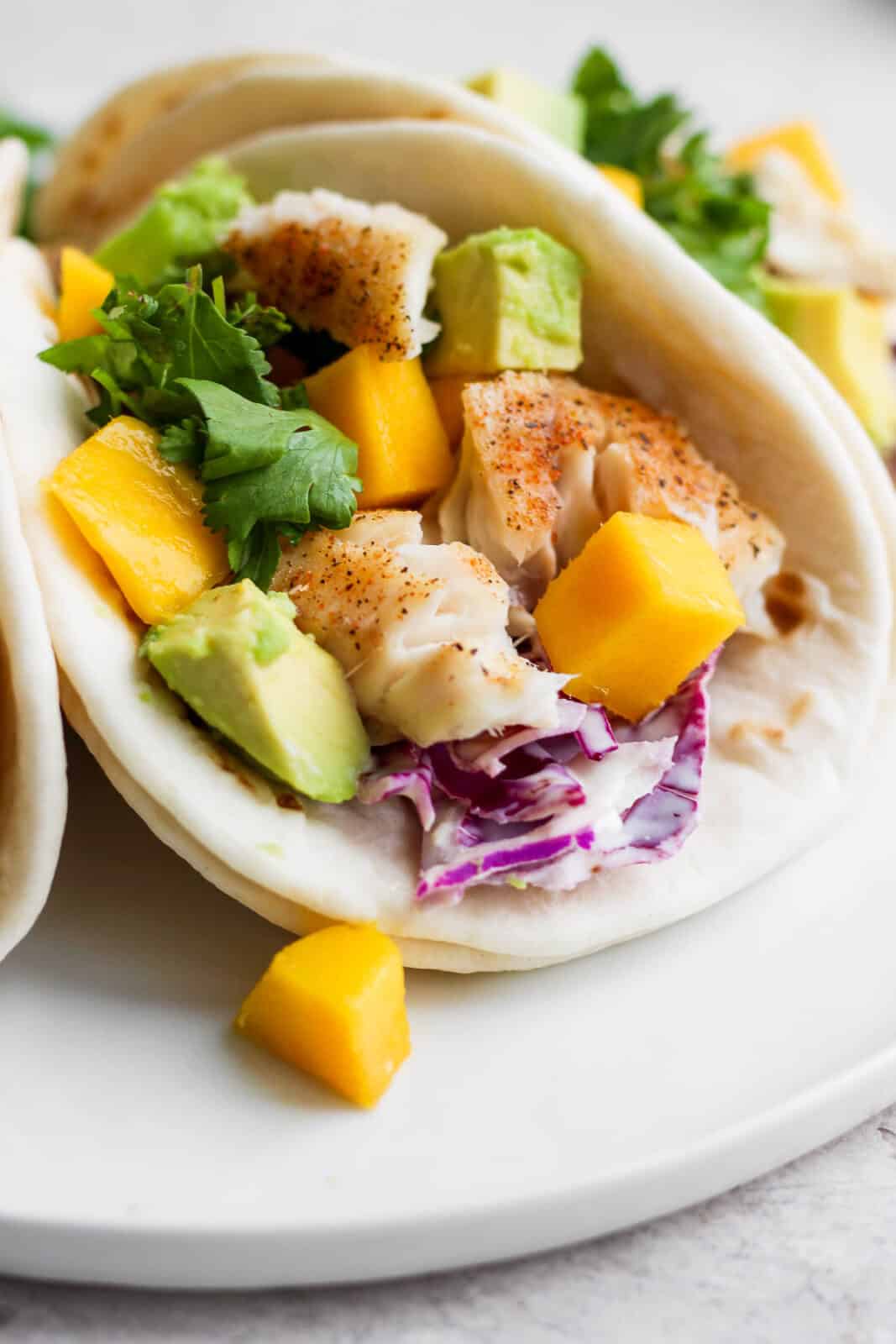 A tilapia fish taco with mango and avocado on a white plate. 