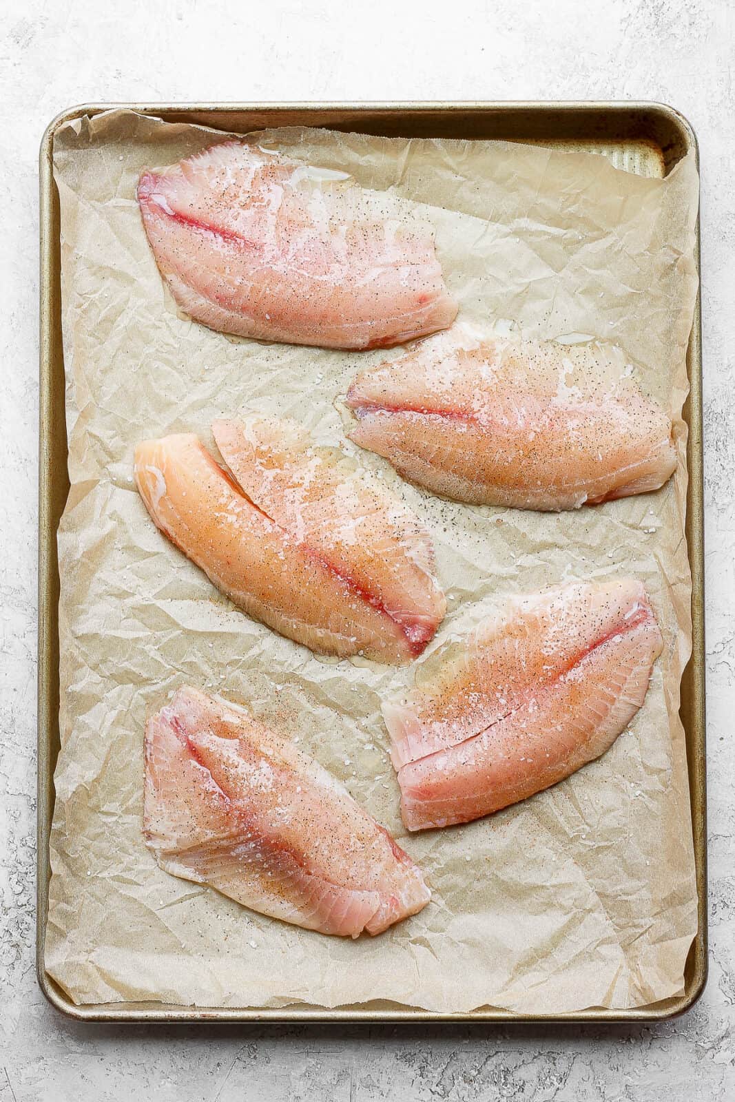 Tilapia on a parchment-lined baking sheet. 