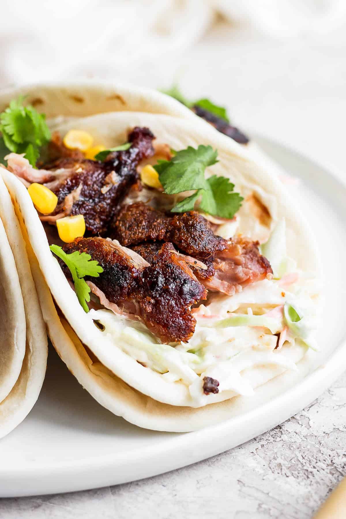 Pork carnitas on a plate with coleslaw, corn and fresh cilantro. 