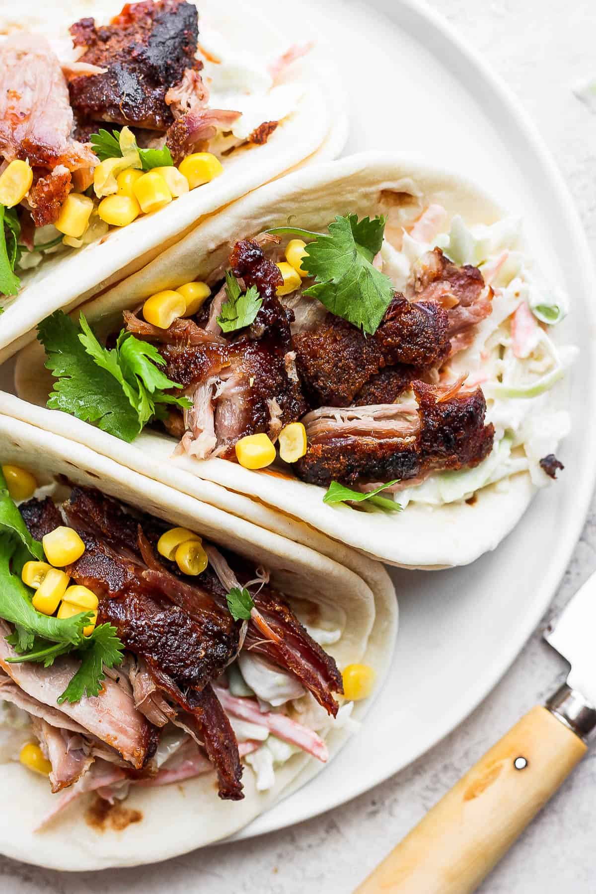 Pork carnitas on a plate with coleslaw, corn and fresh cilantro. 