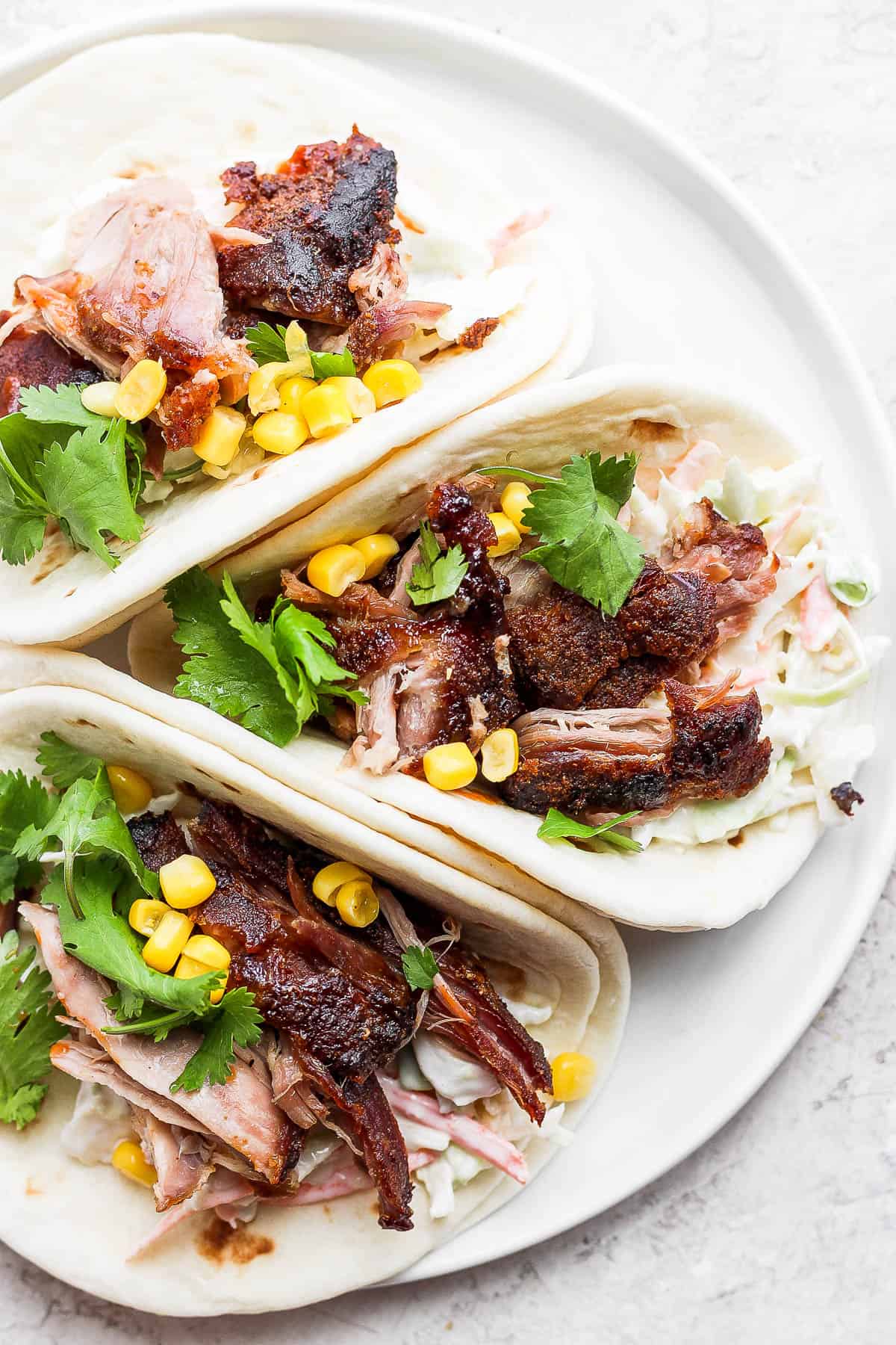 Pork carnitas on a plate with coleslaw, corn and fresh cilantro. 