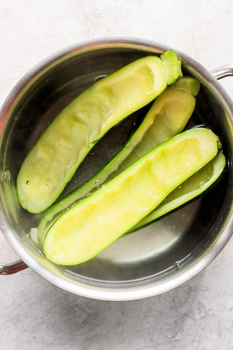 Four zucchini halves being parboiled.