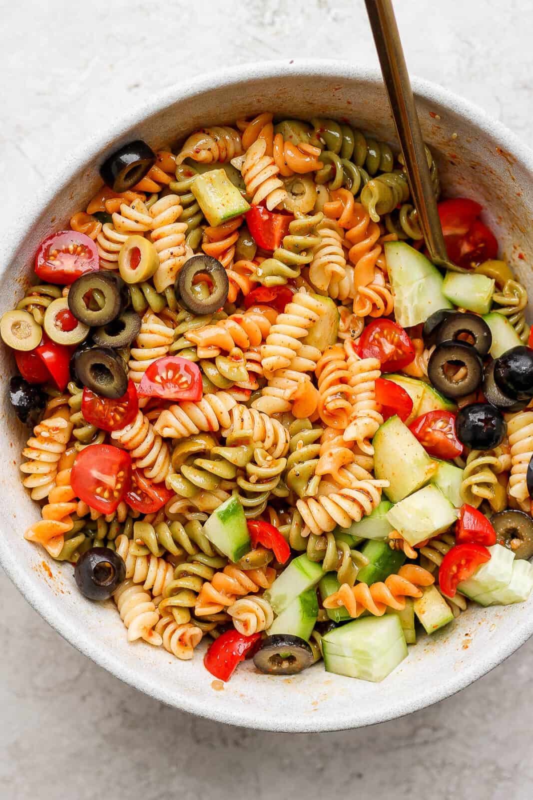 Zesty italian pasta in a bowl with a spoon sticking out. 