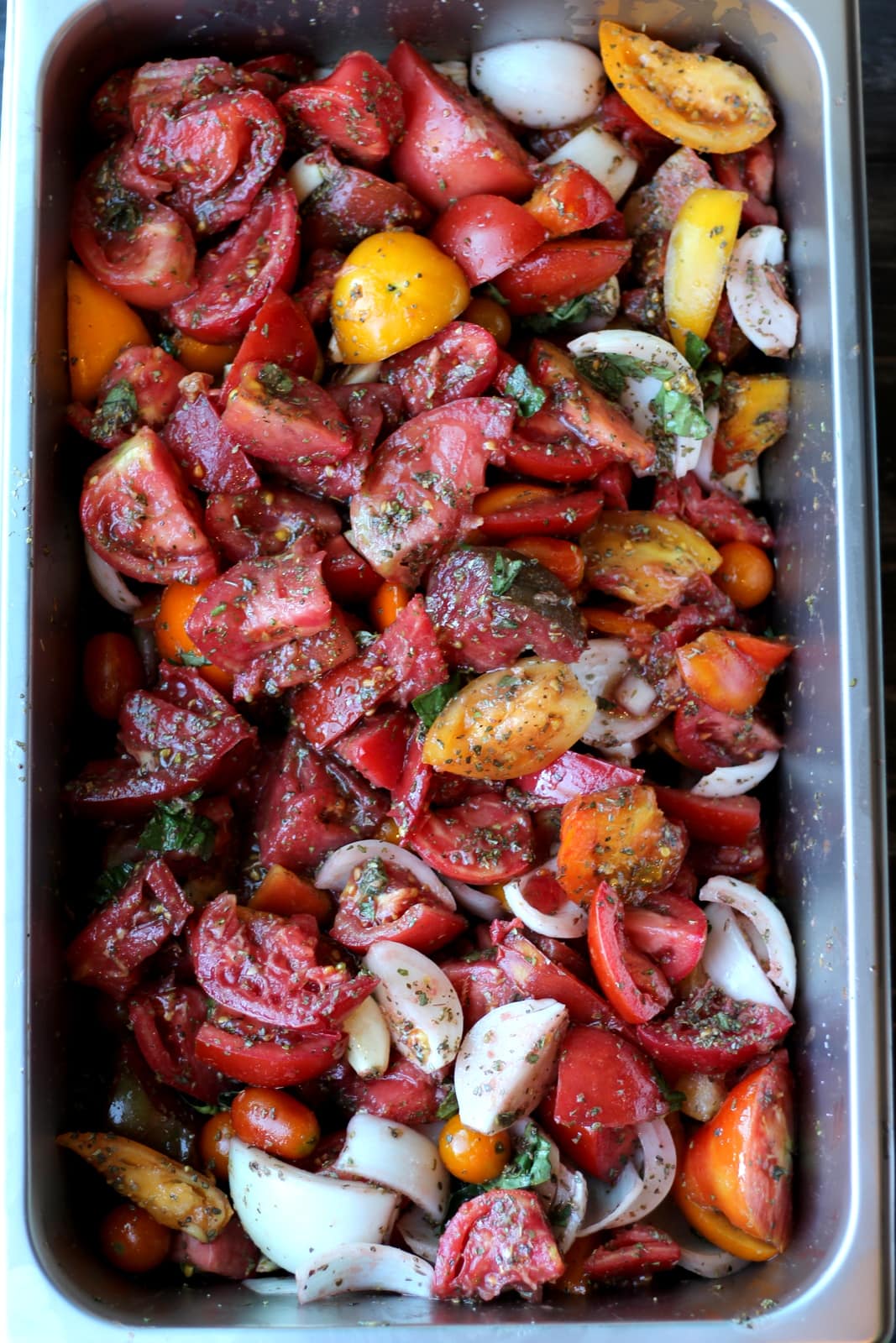 Large aluminum pan filled with fresh tomatoes, herbs and onion. 