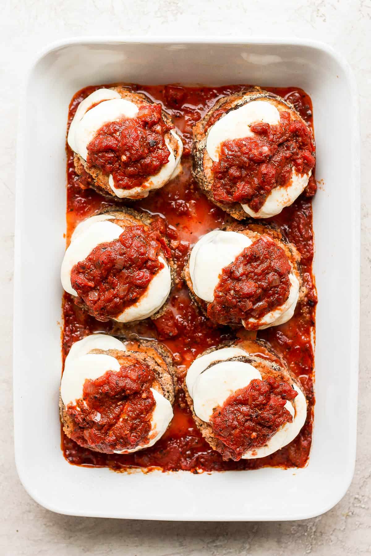 Stacks of eggplant parmesan in a baking dish ready to go in the oven.