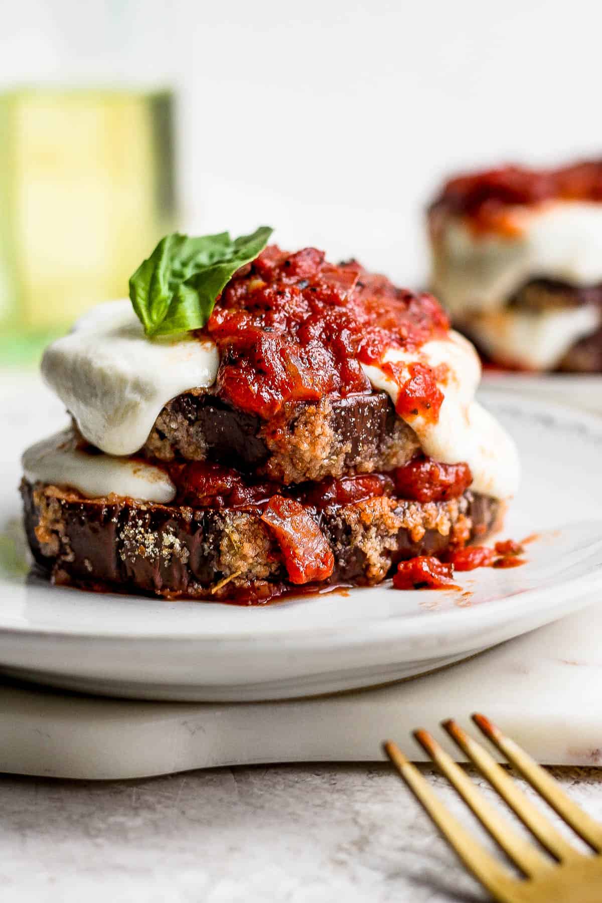 A serving of eggplant parmesan on a white plate with a fork.