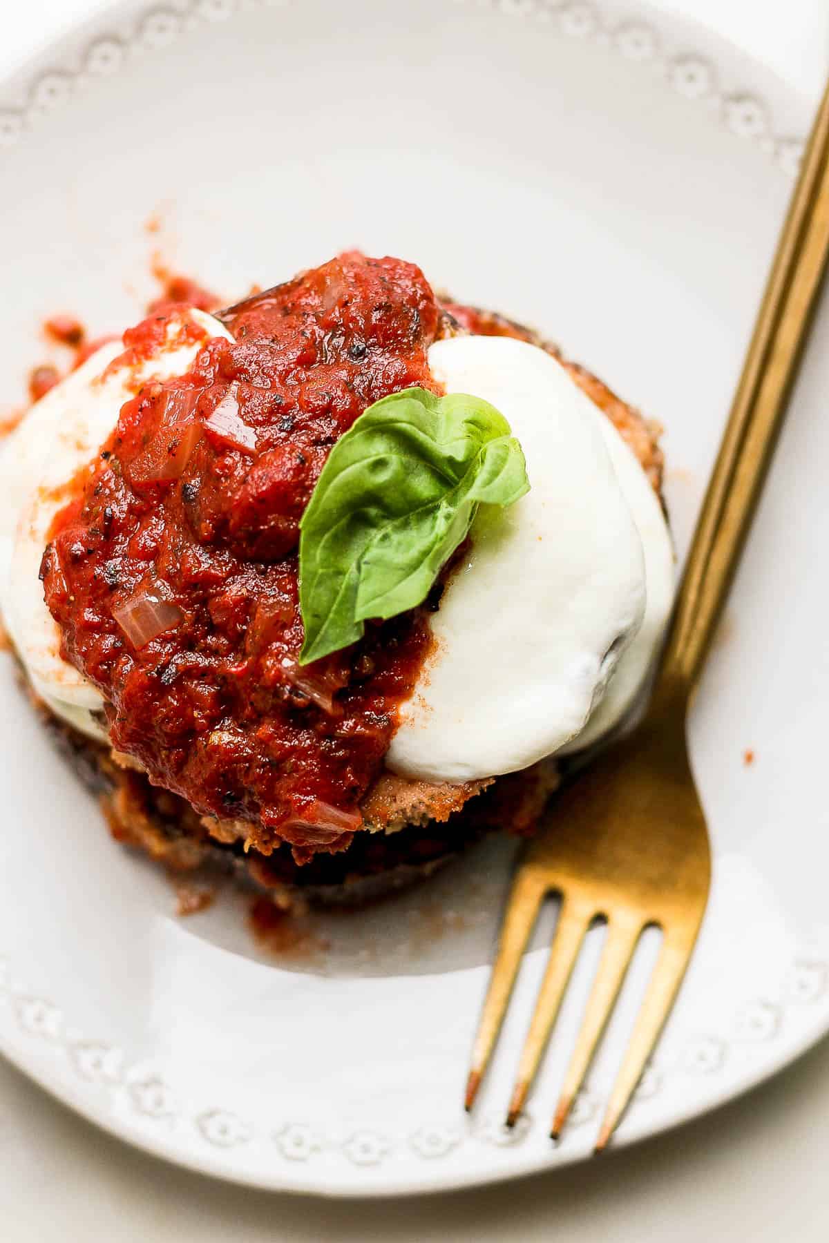 Close up of the top of a stack of baked eggplant parmesan with a fresh basil leaf on top. 