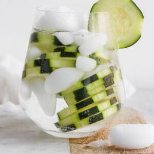 A cocktail glass with a cucumber vodka and water over ice and garnished with fresh cucumber slices.