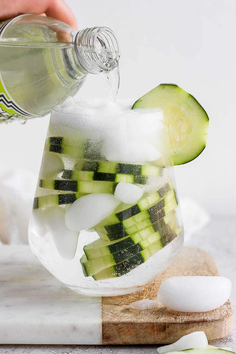 Someone pouring tonic into a cucumber vodka and water.