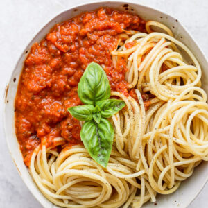 A bowl of noodles with homemade marinara sauce garnished with fresh basil.
