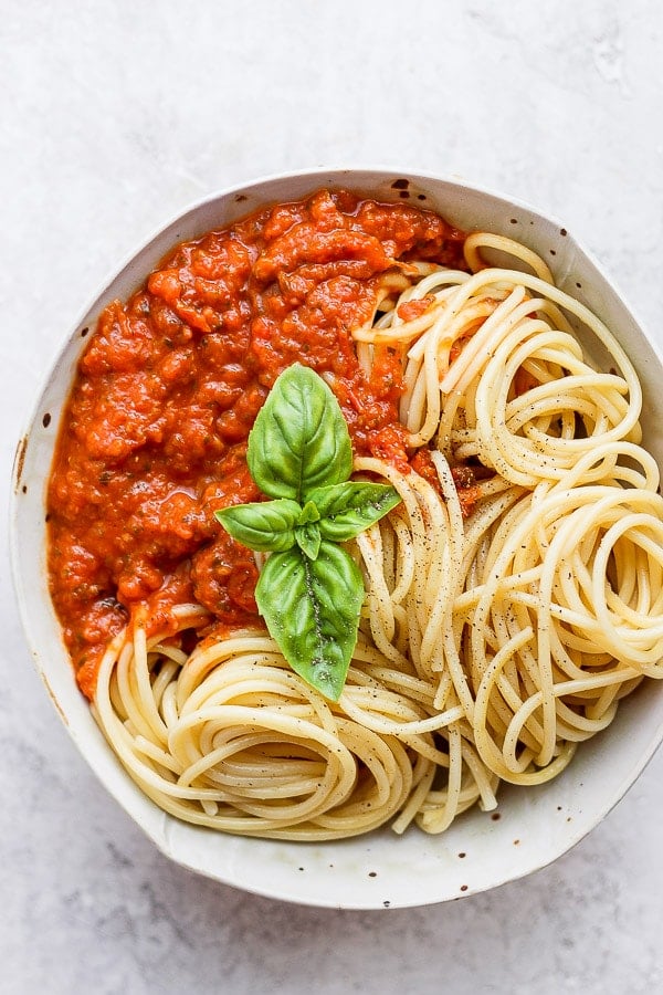 Bowl of homemade marinara sauce, noodles and fresh basil leaves.