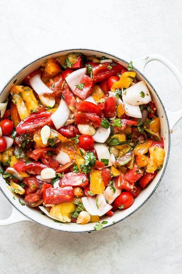 Dutch oven filled with tomatoes, garlic, onions and herbs. 