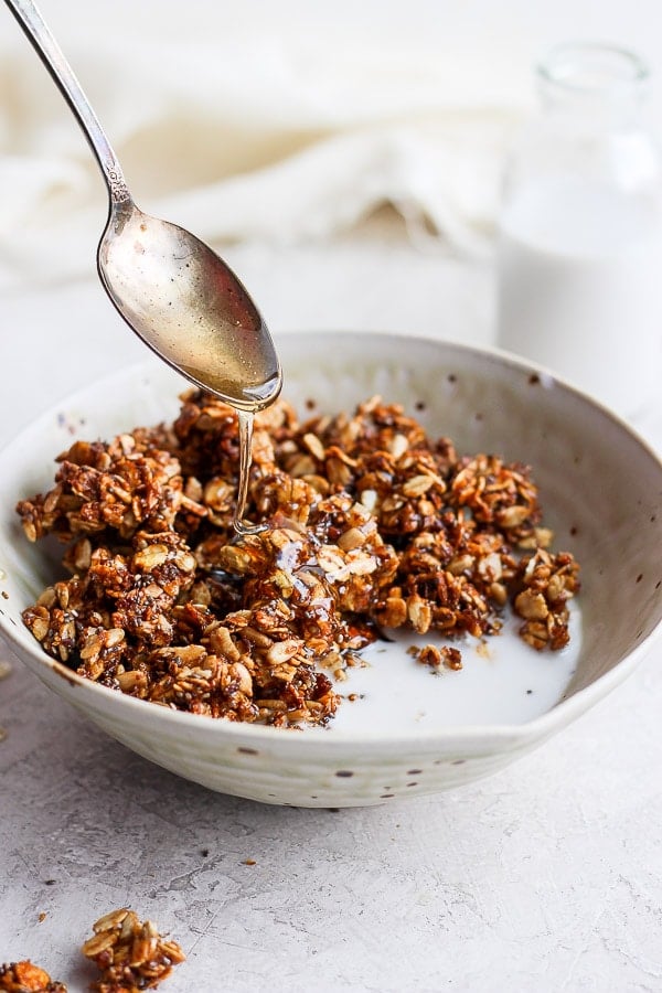 A spoon drizzling honey over some granola in a bowl with milk.