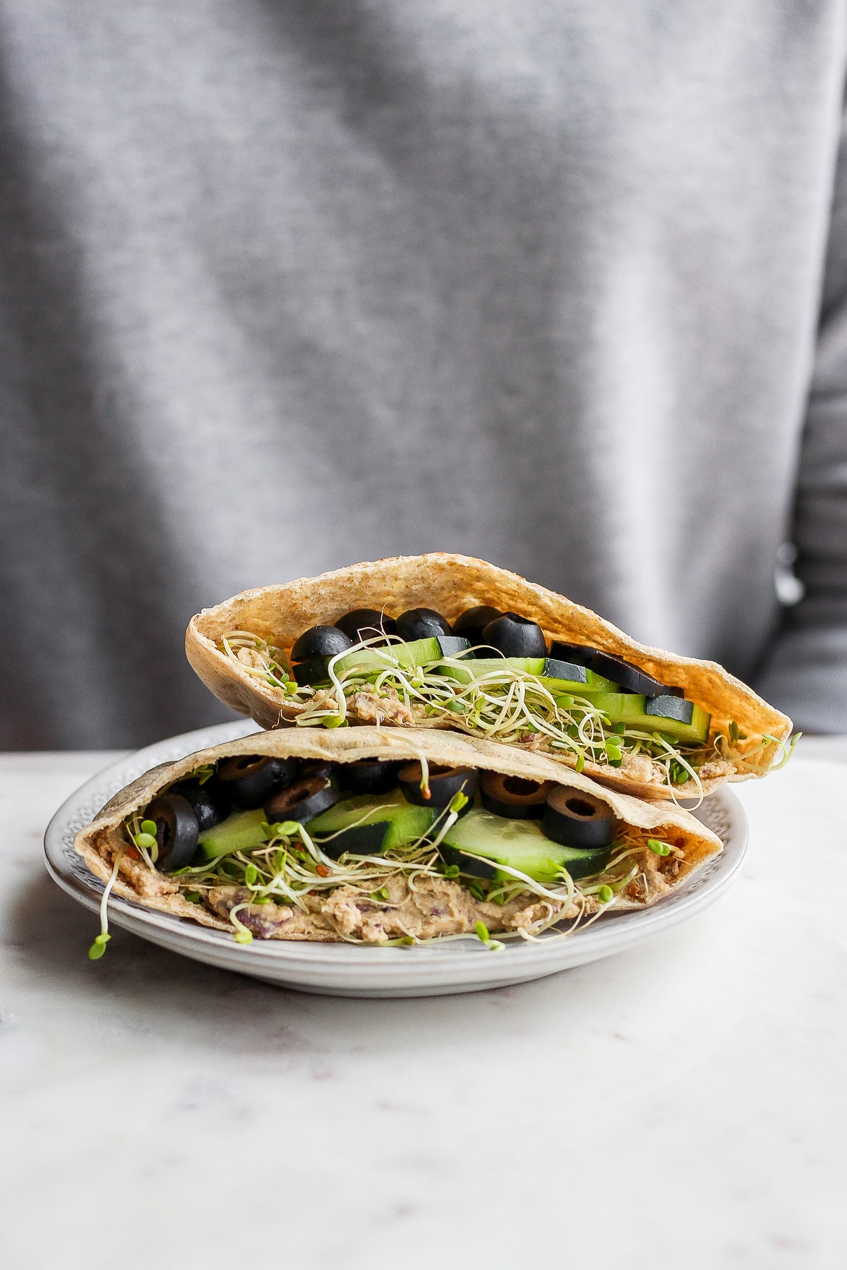 A vegan pita sandwich sitting on a plate in from of someone. 