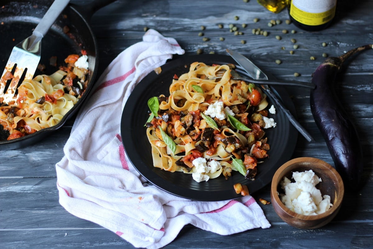 Eggplant ragu on a plate and some in the skillet with a bowl of cheese chunks on the side.