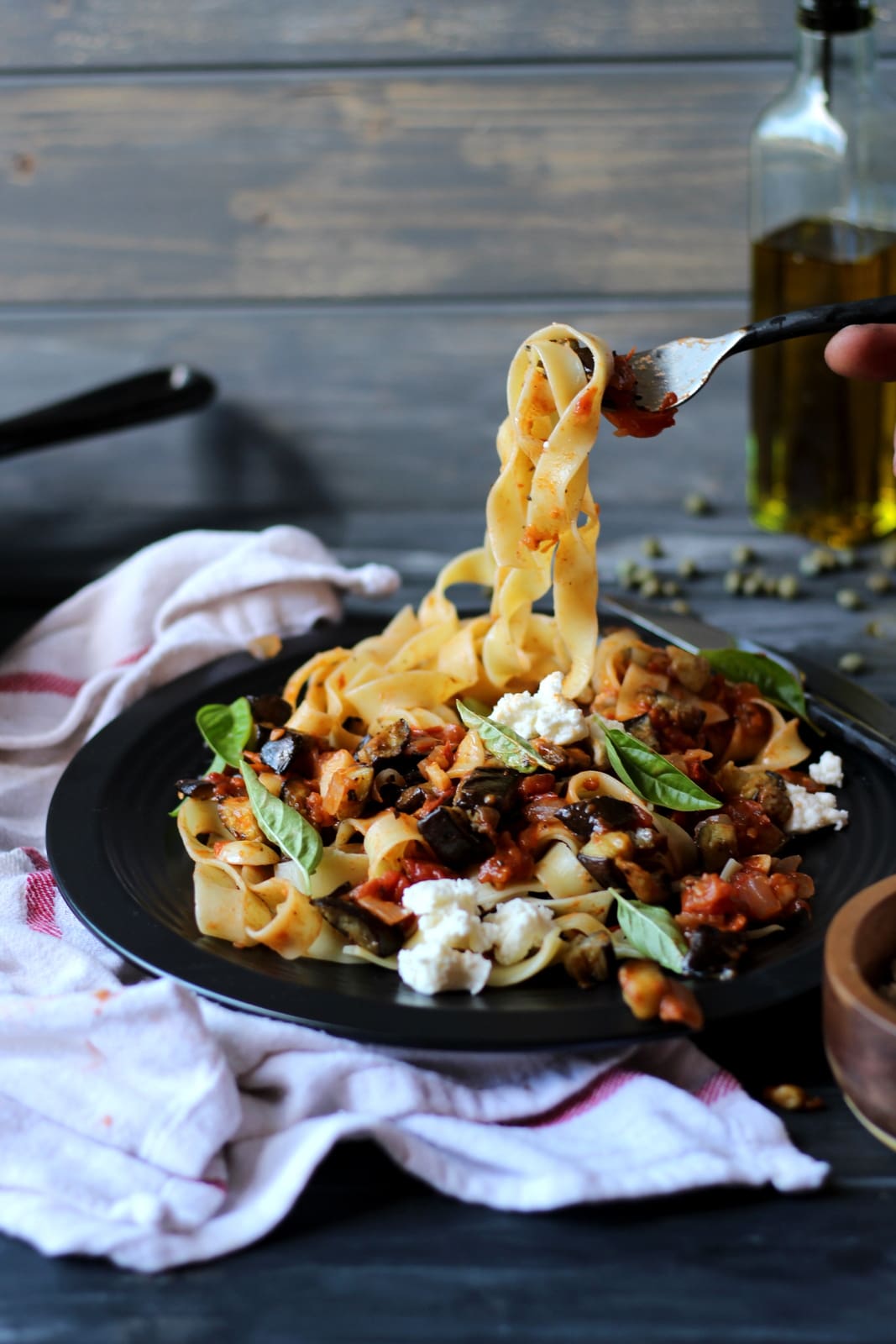 Eggplant ragu on a black plate and a fork pulling some of the noodles up.