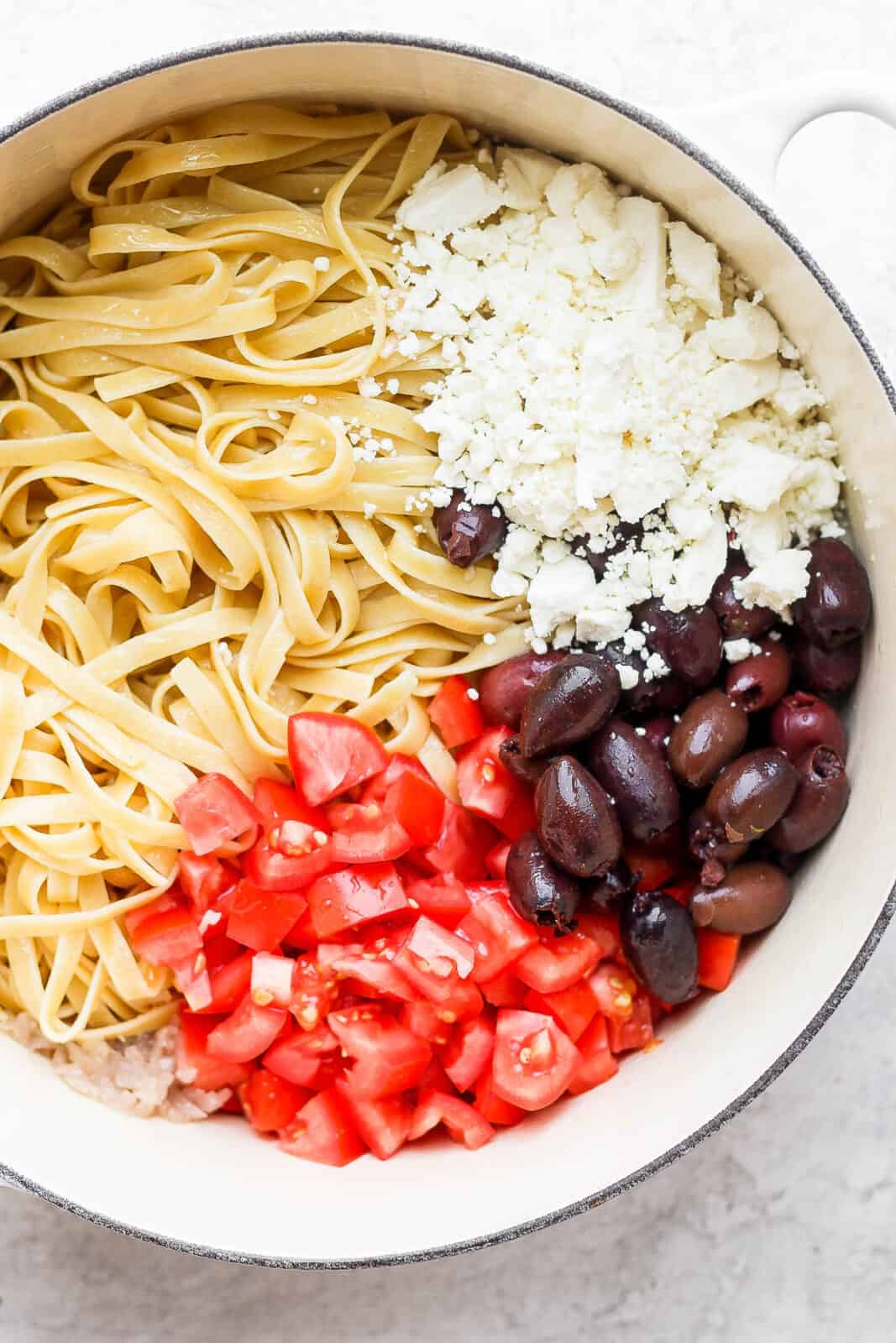 Pan of cooked noodles with feta, olives and tomato. 