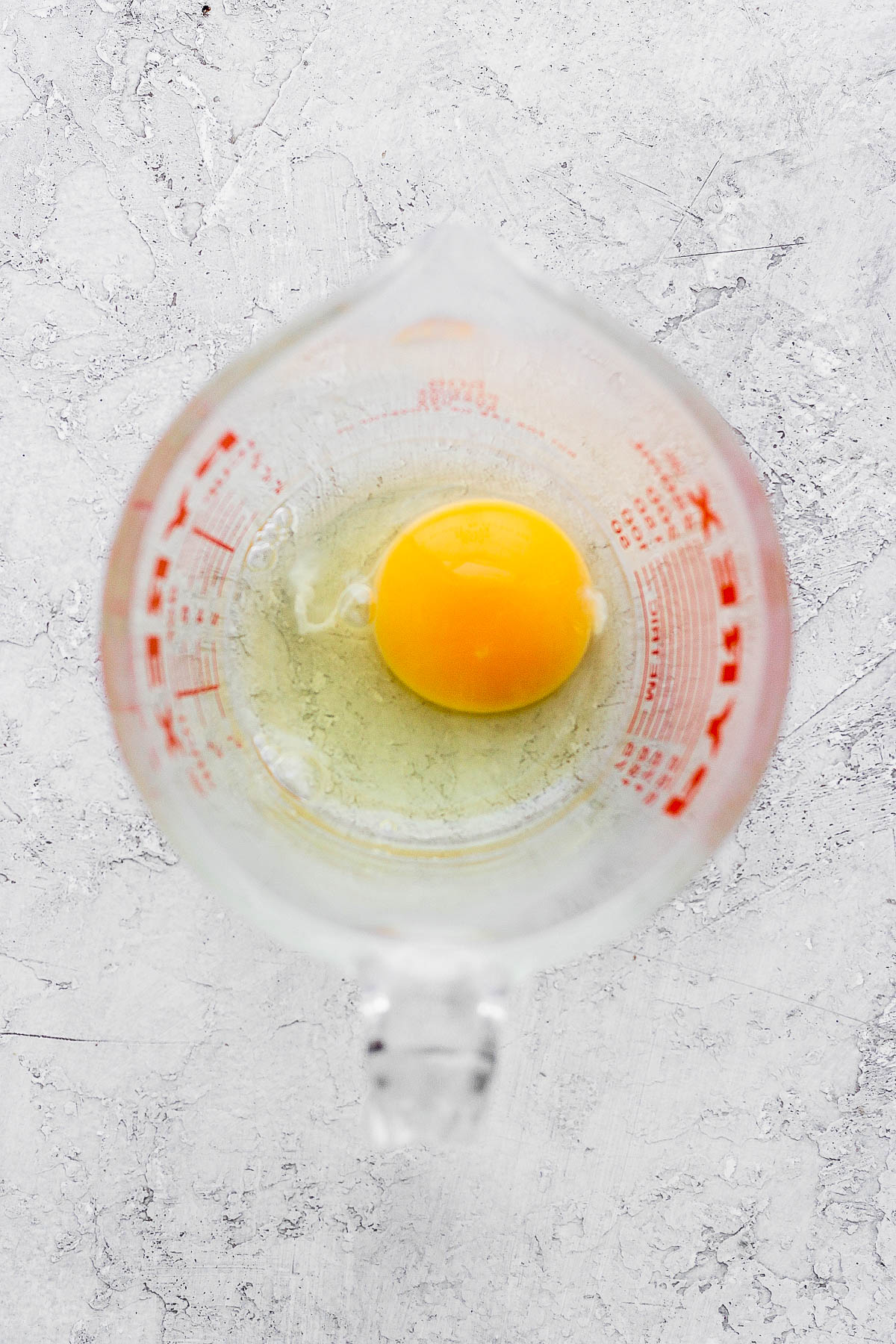 A raw egg in a glass measuring cup. 