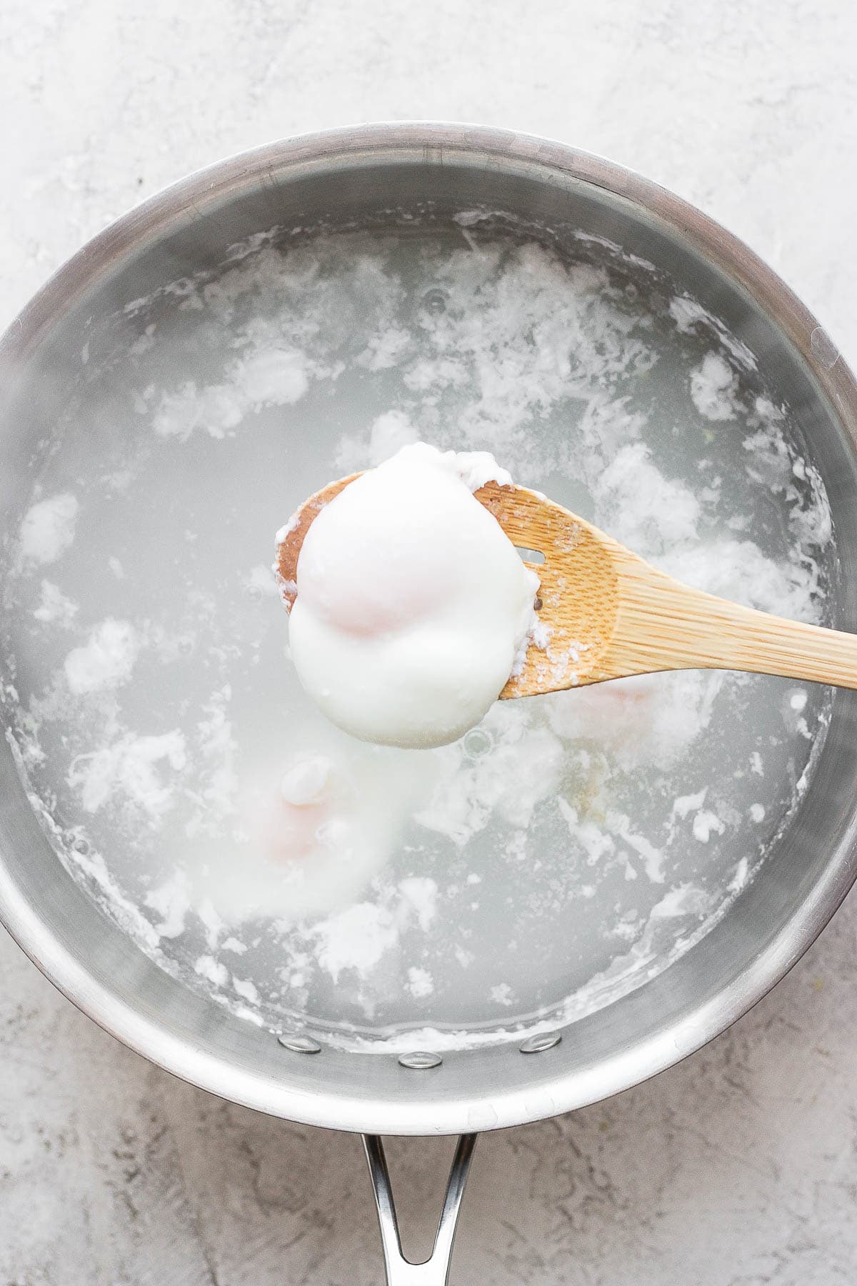 A poached egg being pulled from a sauce pan filled with water to top onto homemade corned beef hash.