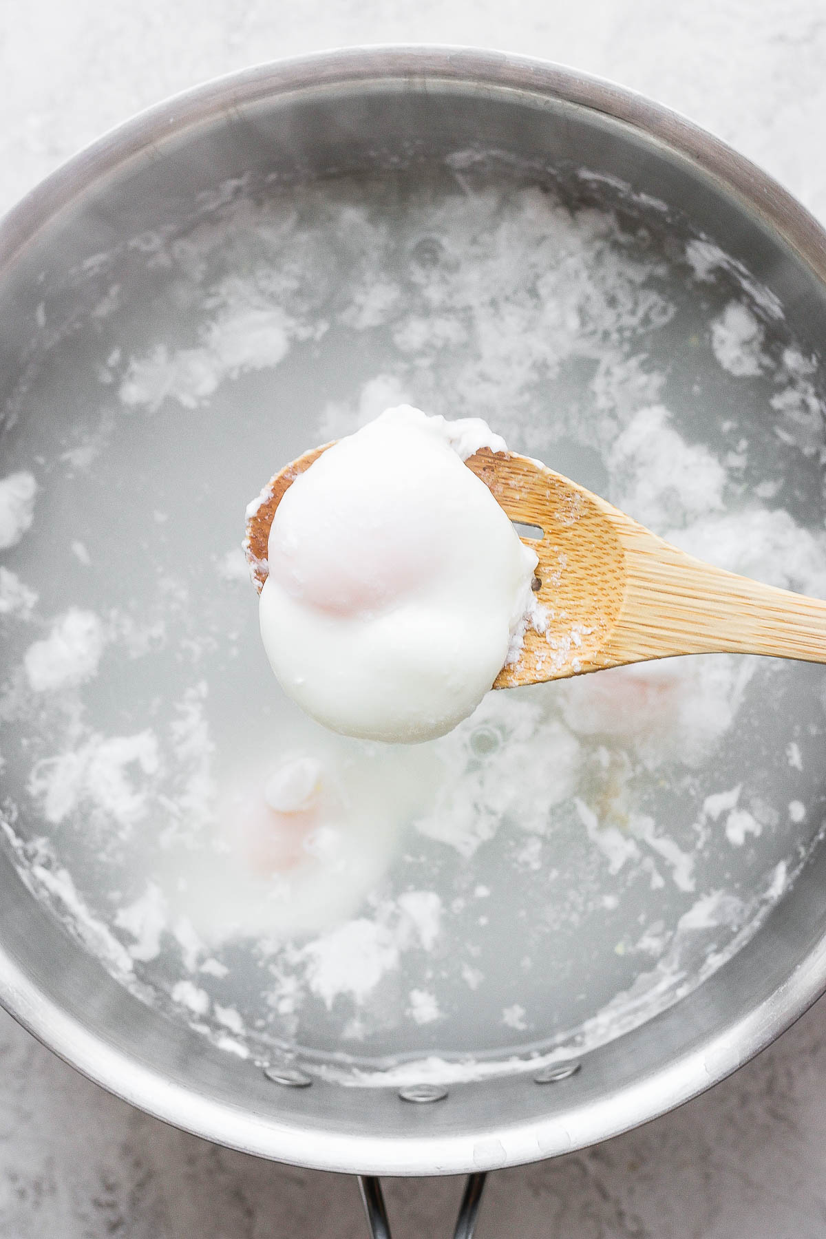 A slotted spoon scooping a poached egg out of the hot water.