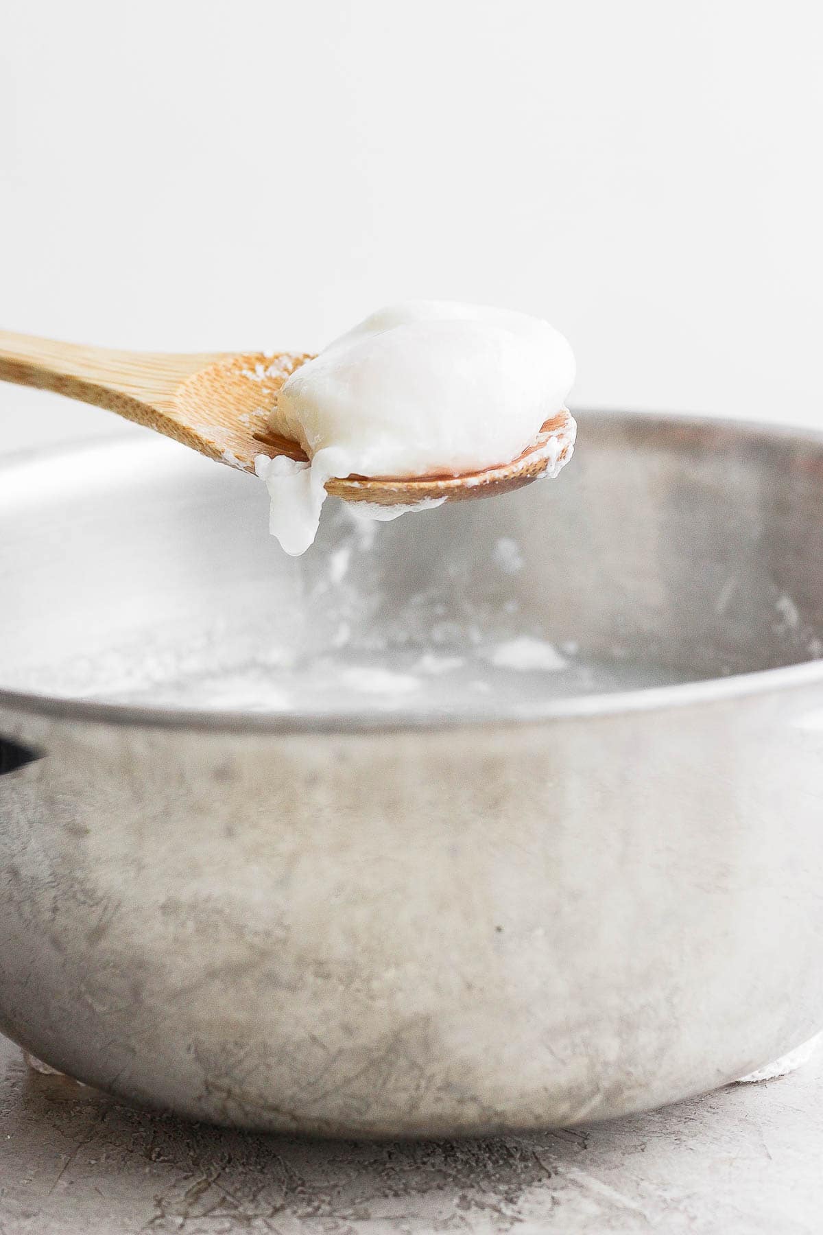 A slotted spoon lifting a poached egg out of a saucepan. 