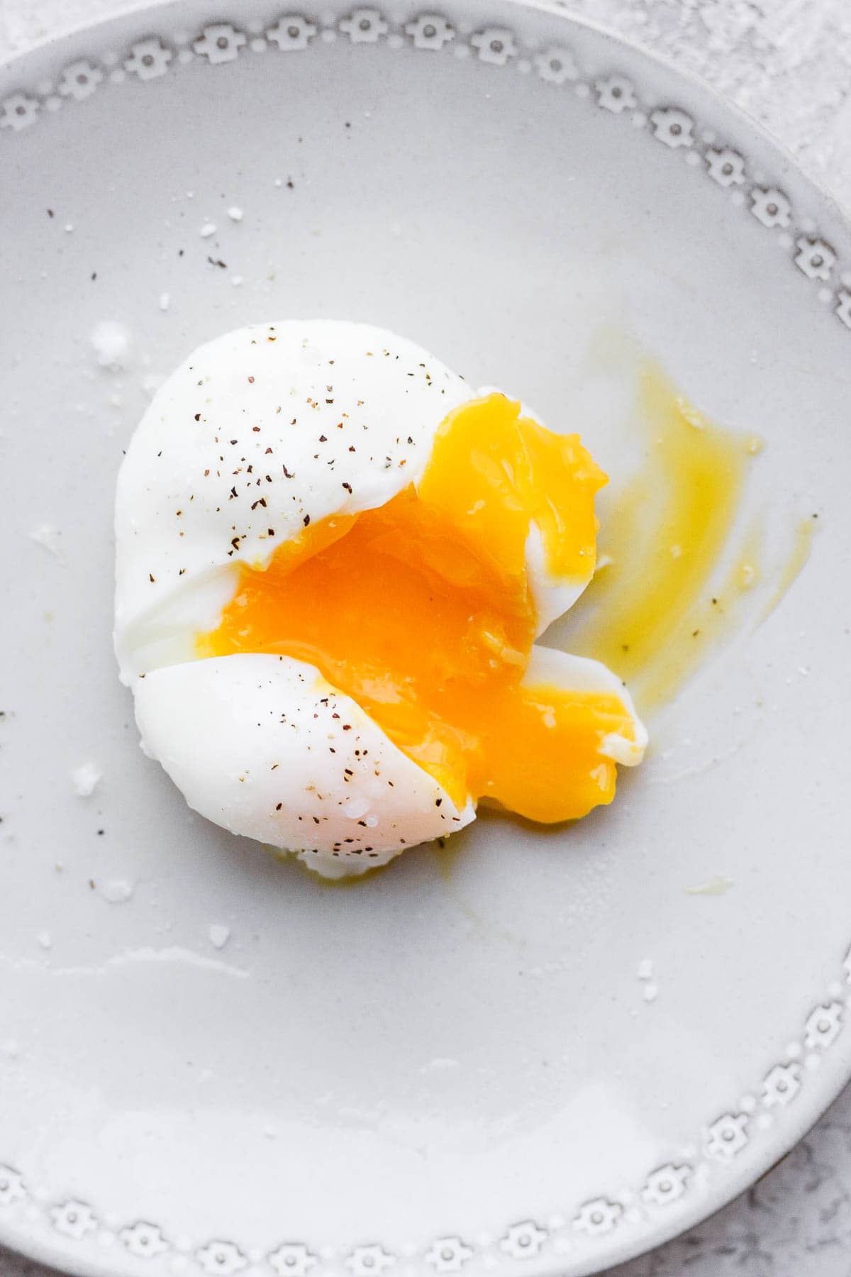 A poached egg on a plate, cut open with the yolk coming out. 