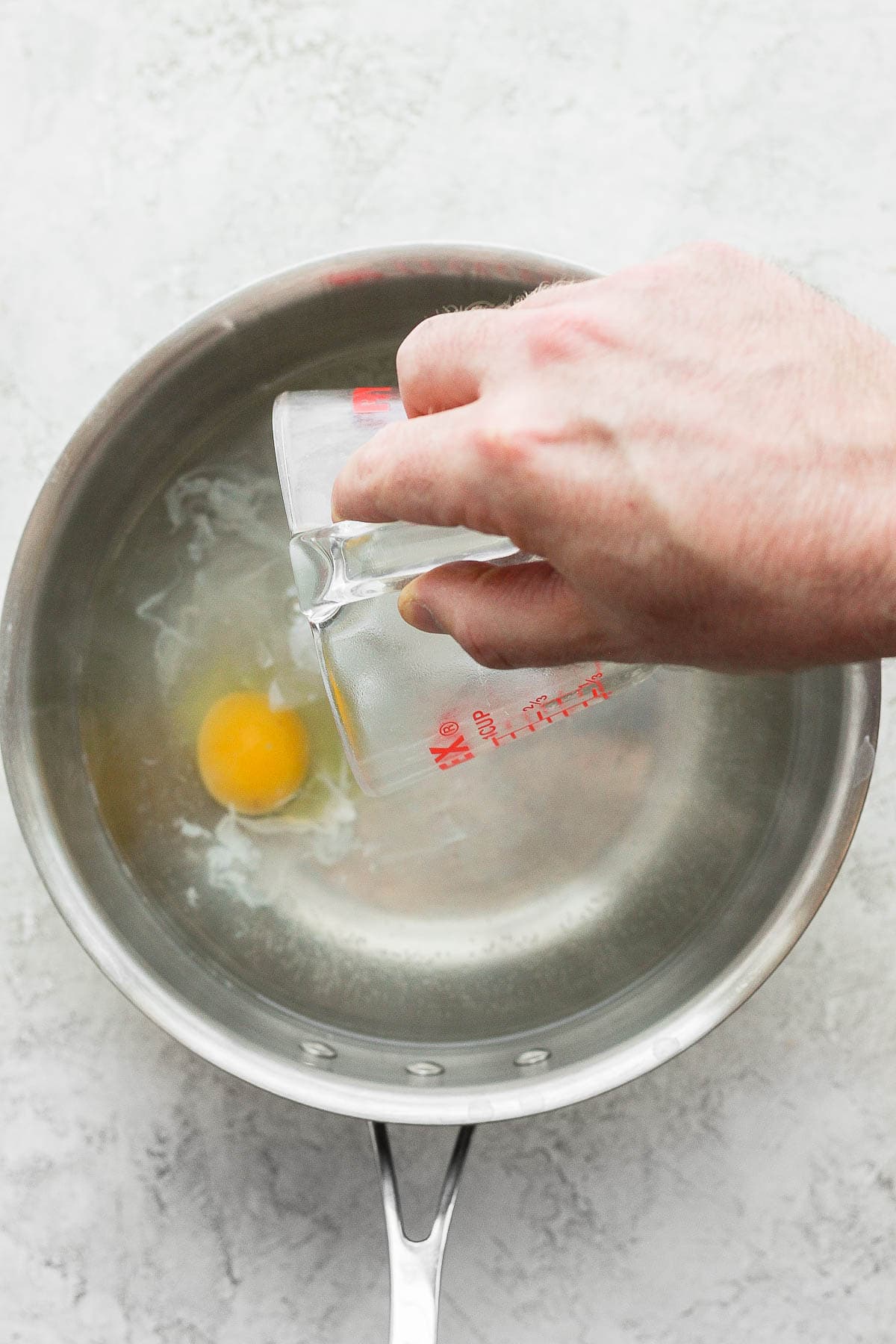 A hand pouring a raw egg into a saucepan. 