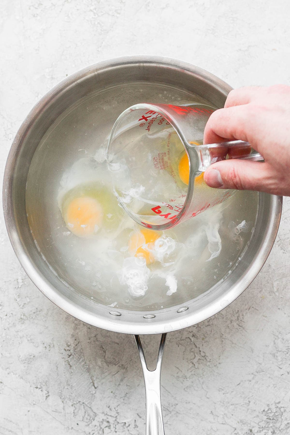 A hand pouring raw eggs into a saucepan. 