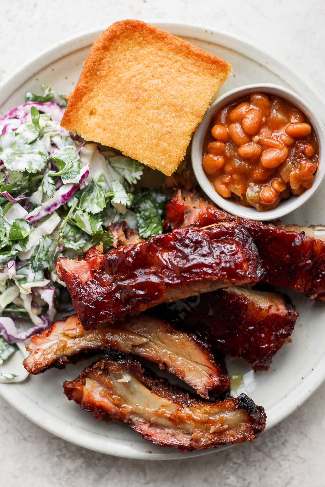 A plate of smoked baby back ribs with coleslaw, beans and cornbread. 