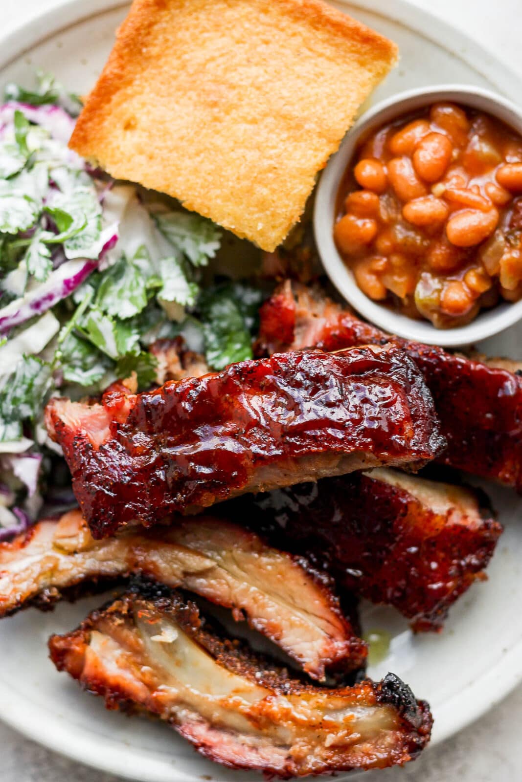Smoked baby back ribs, smoked baked beans, cornbread, and spicy purple cabbage coleslaw on a plate.