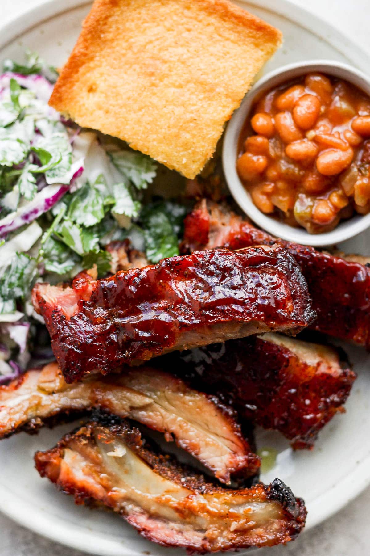 A plate filled with smoked baby back ribs, smoked beans, coleslaw and cornbread. 