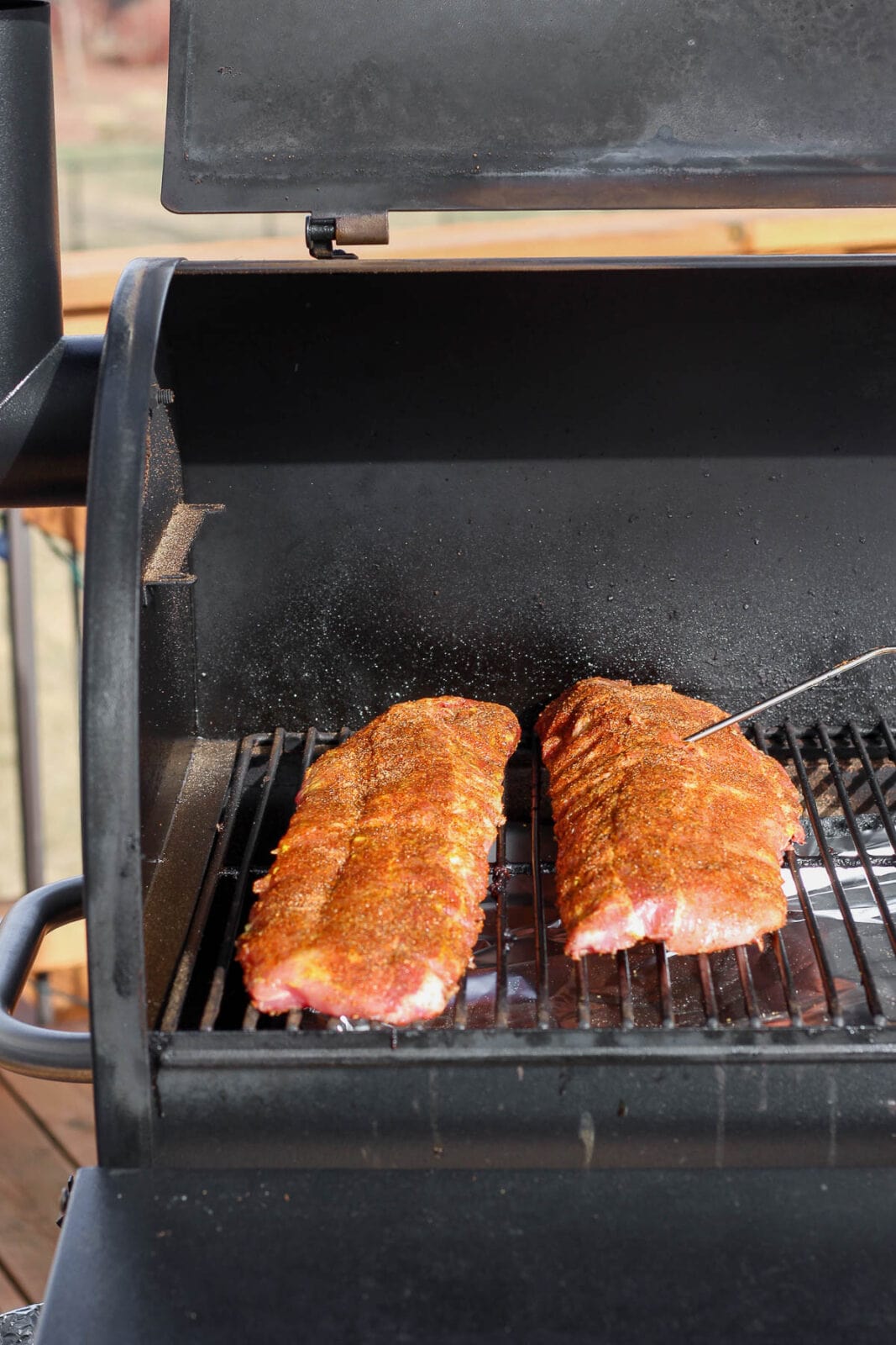 Two racks of ribs on the smoker with a probe sticking out of one of them. 