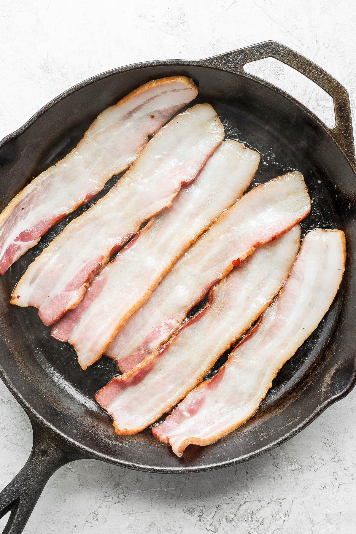 Six pieces of bacon cooking in a cast iron skillet. 