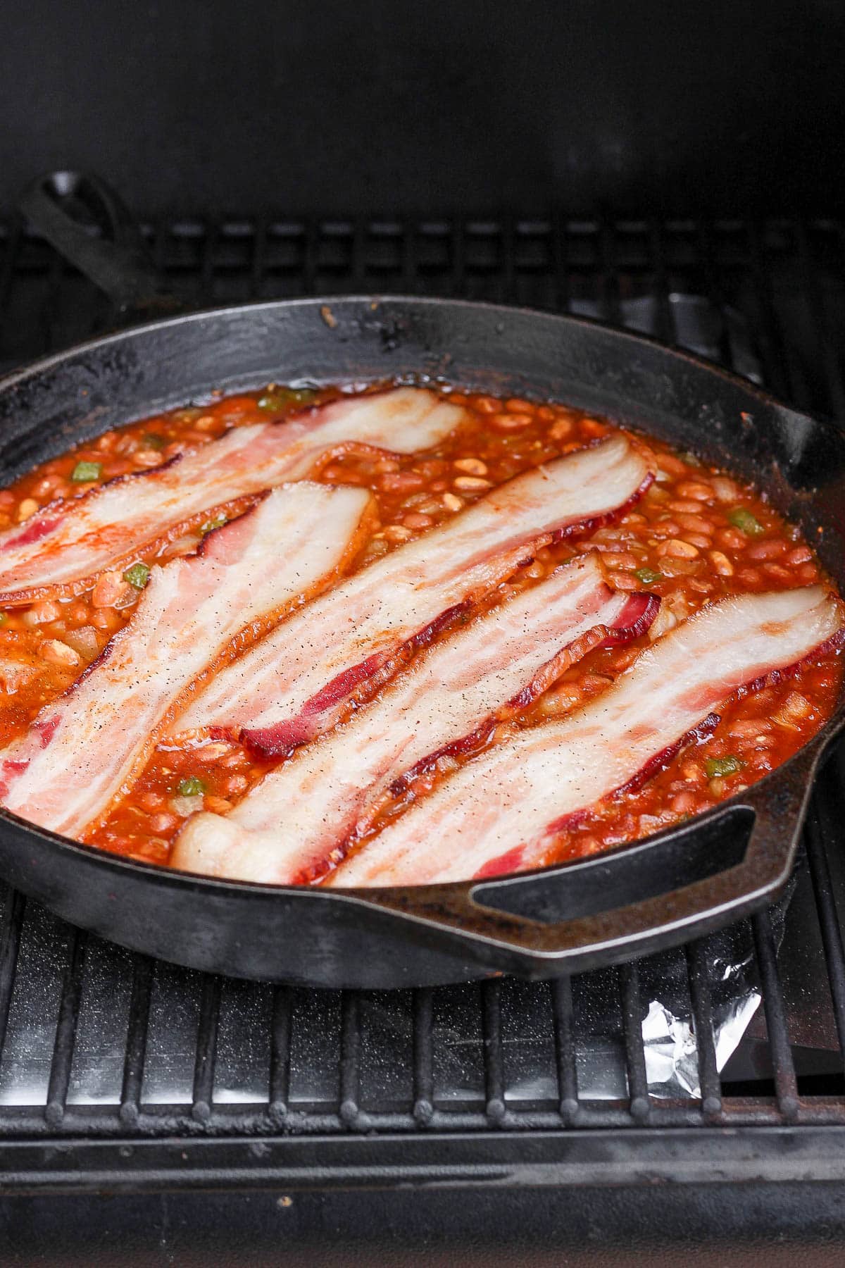 Baked beans being smoked in a cast iron skillet. 