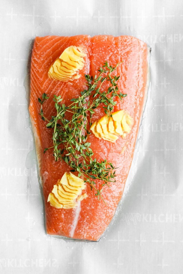 A piece of salmon with ghee, salt and fresh thyme on top of it. 