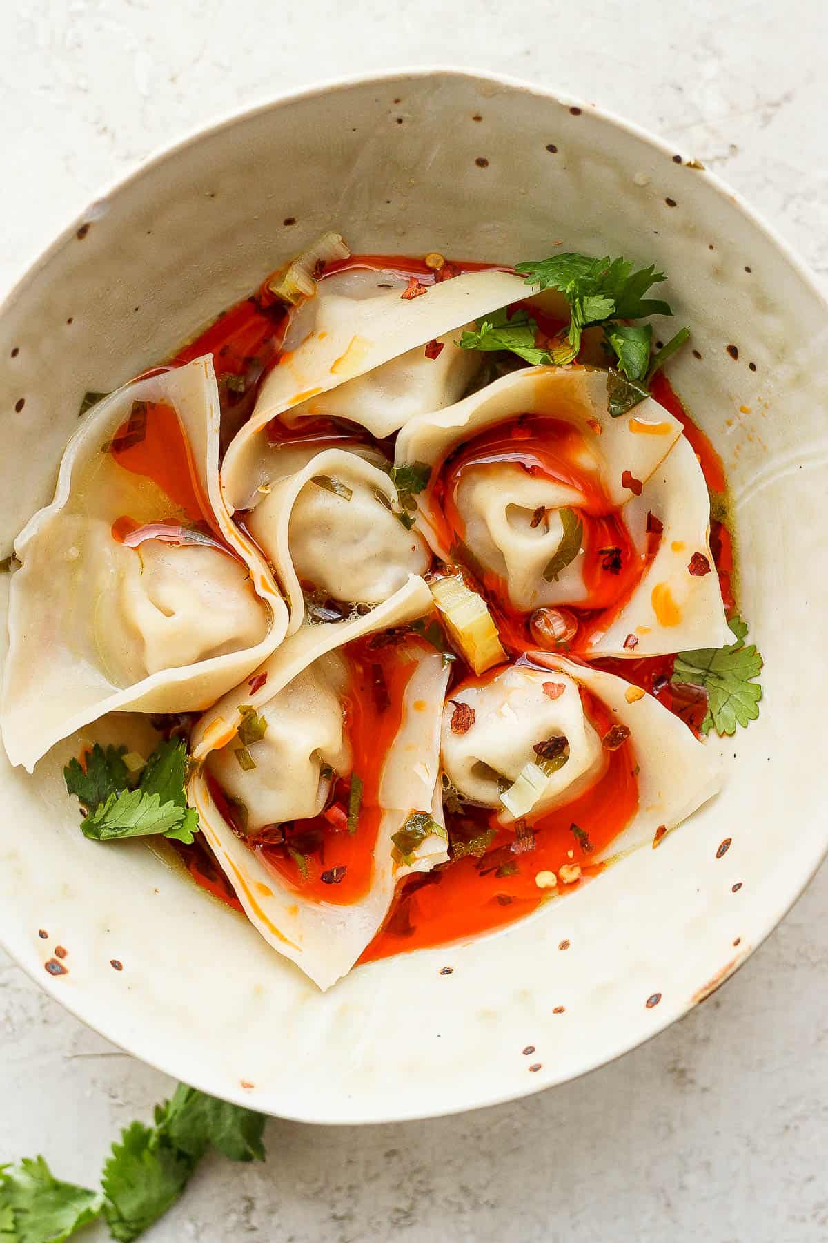 Bowl of spicy pork wontons garnished with some fresh cilantro. 