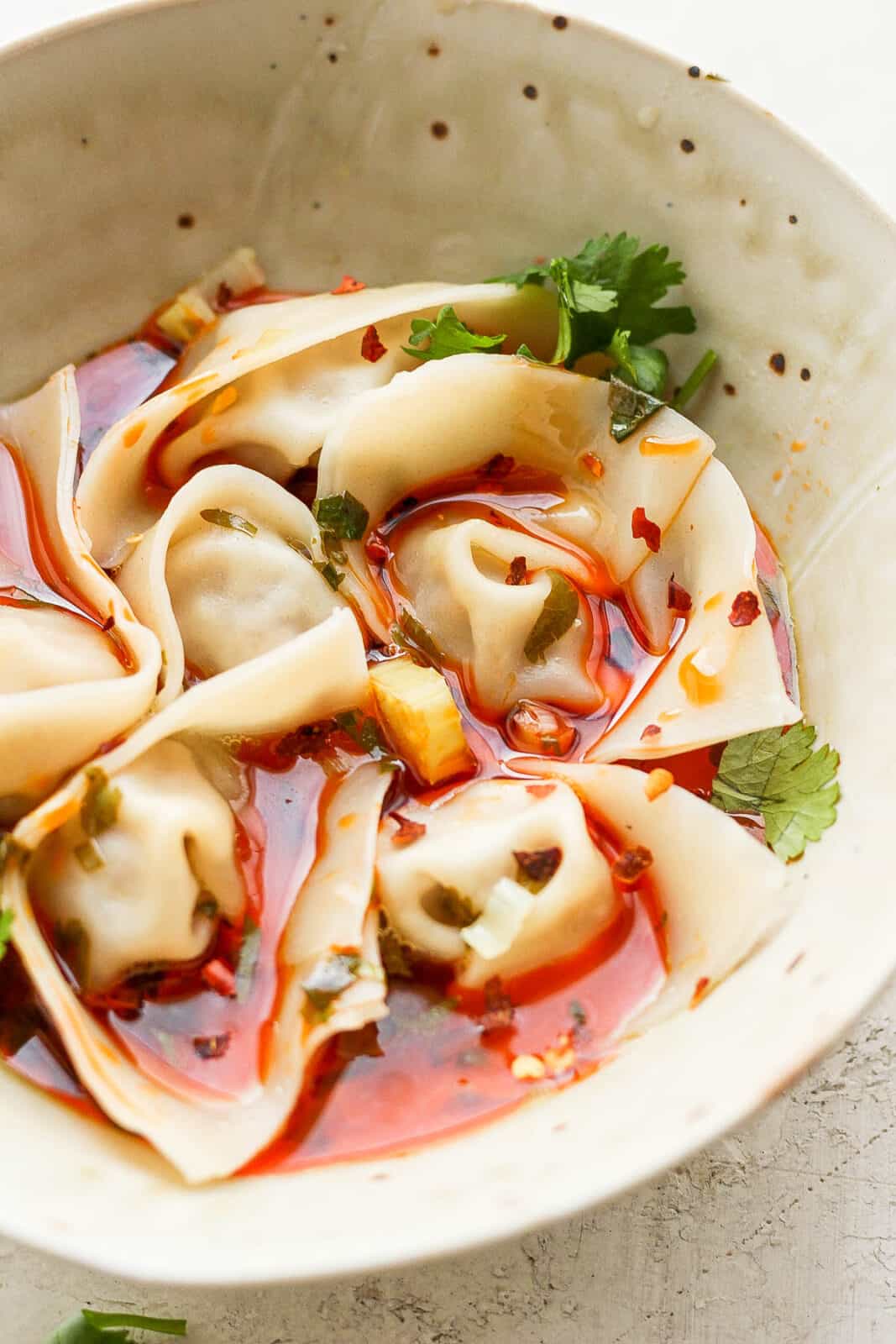 Side view of a bowl of spicy pork wontons covered in red chili broth.