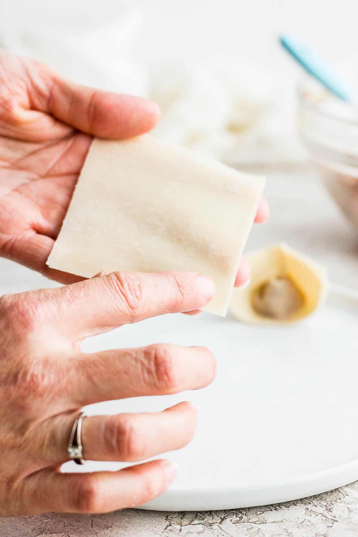 Someone wetting the edges of a wonton wrapper with water on their finger.