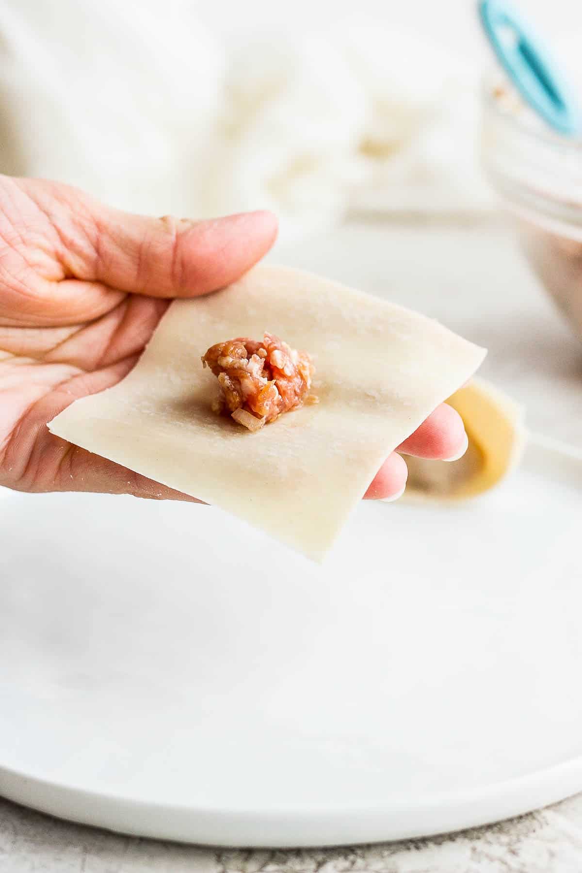 A teaspoon of pork filling in the middle of a wonton wrapper.