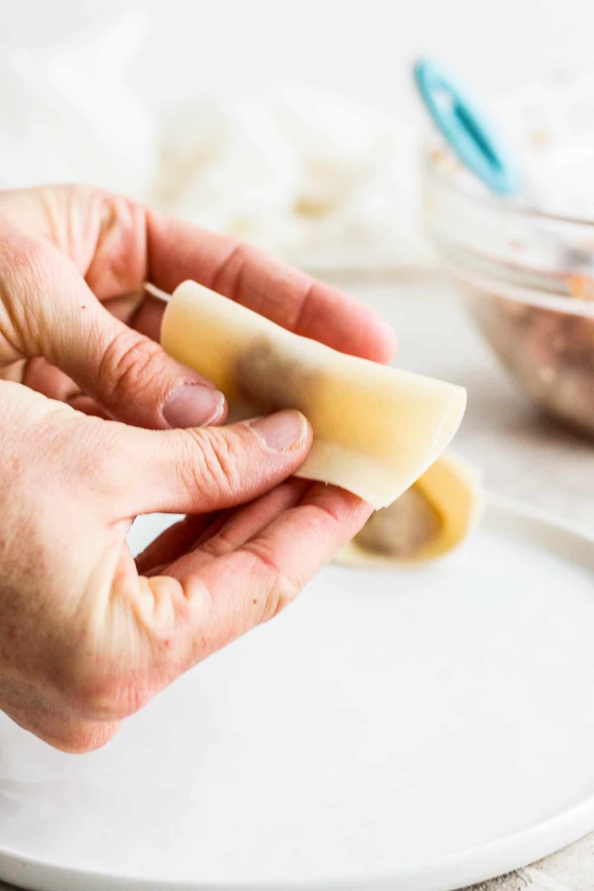 Someone folding over the wonton wrapper in half over the pork filling. 