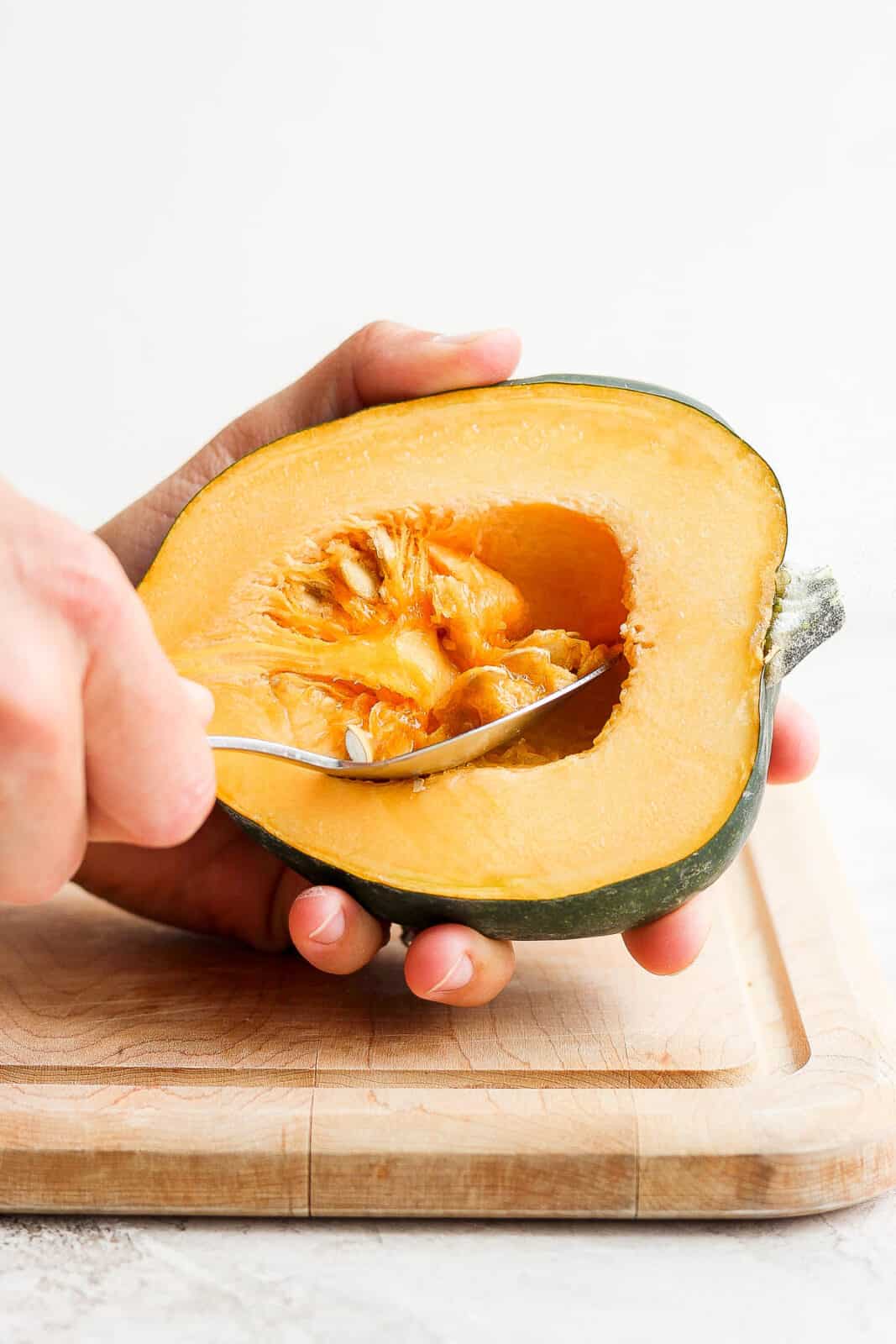 A halved acorn squash with someone scooping out the seeds.