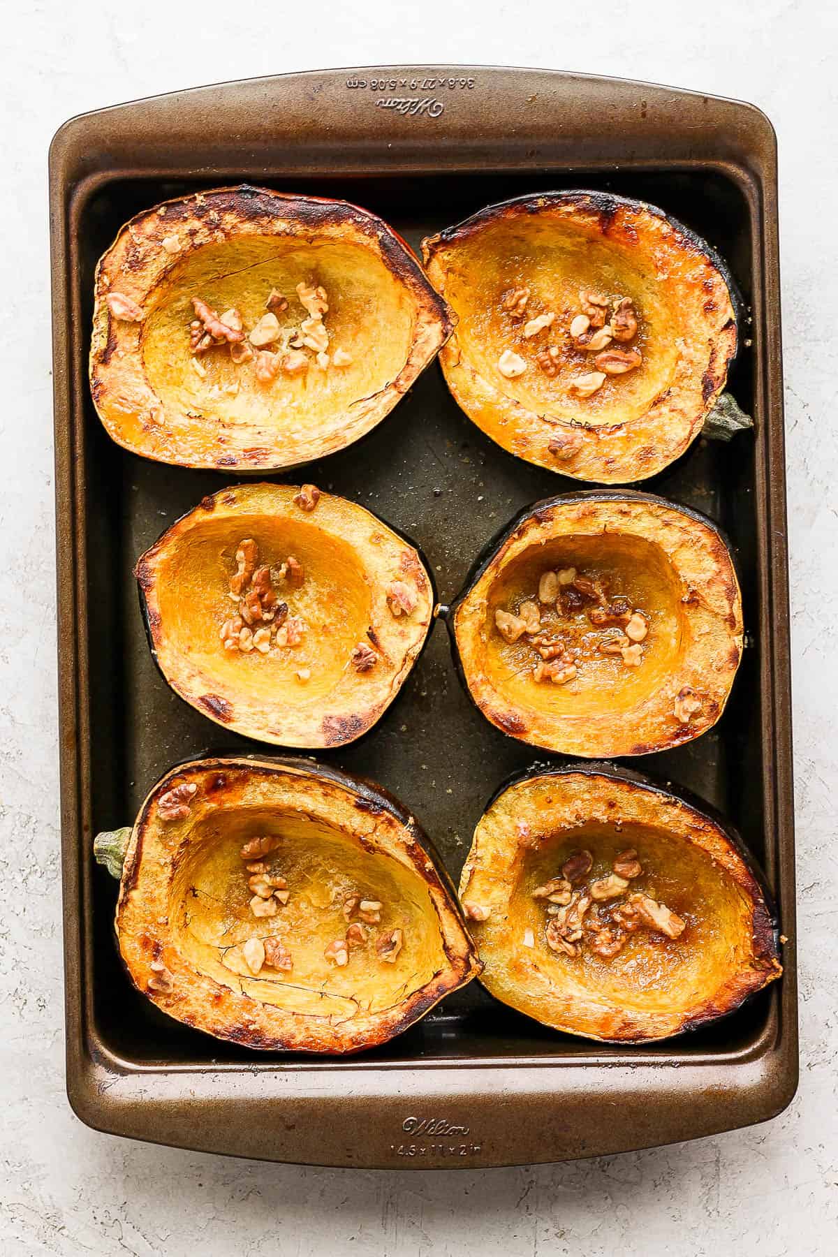 A pan of roasted acorn squash with brown butter and walnuts in the middle. 