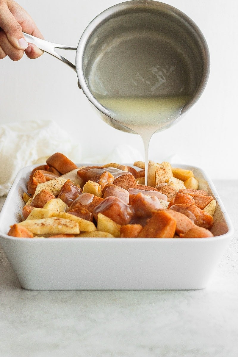 Casserole dish with apple yam bake inside and pouring sauce on top. 