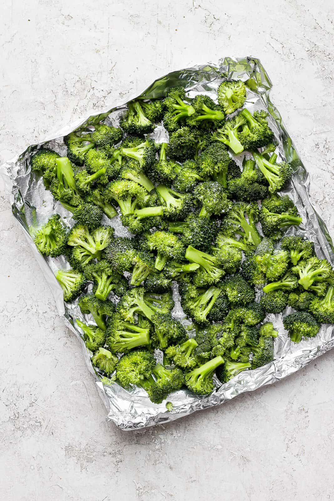 Broccoli florets in an aluminum foil boat after being coated in olive oil and salt sprinkled on top.