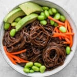 Bowl of soba noodles with carrots, edamame and avocado.