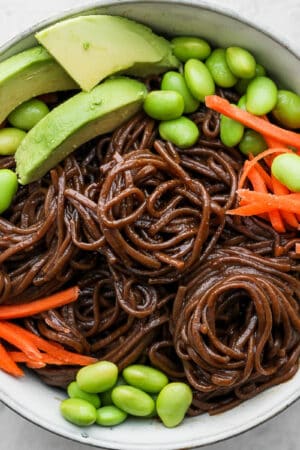 Bowl of soba noodles with carrots, edamame and avocado.