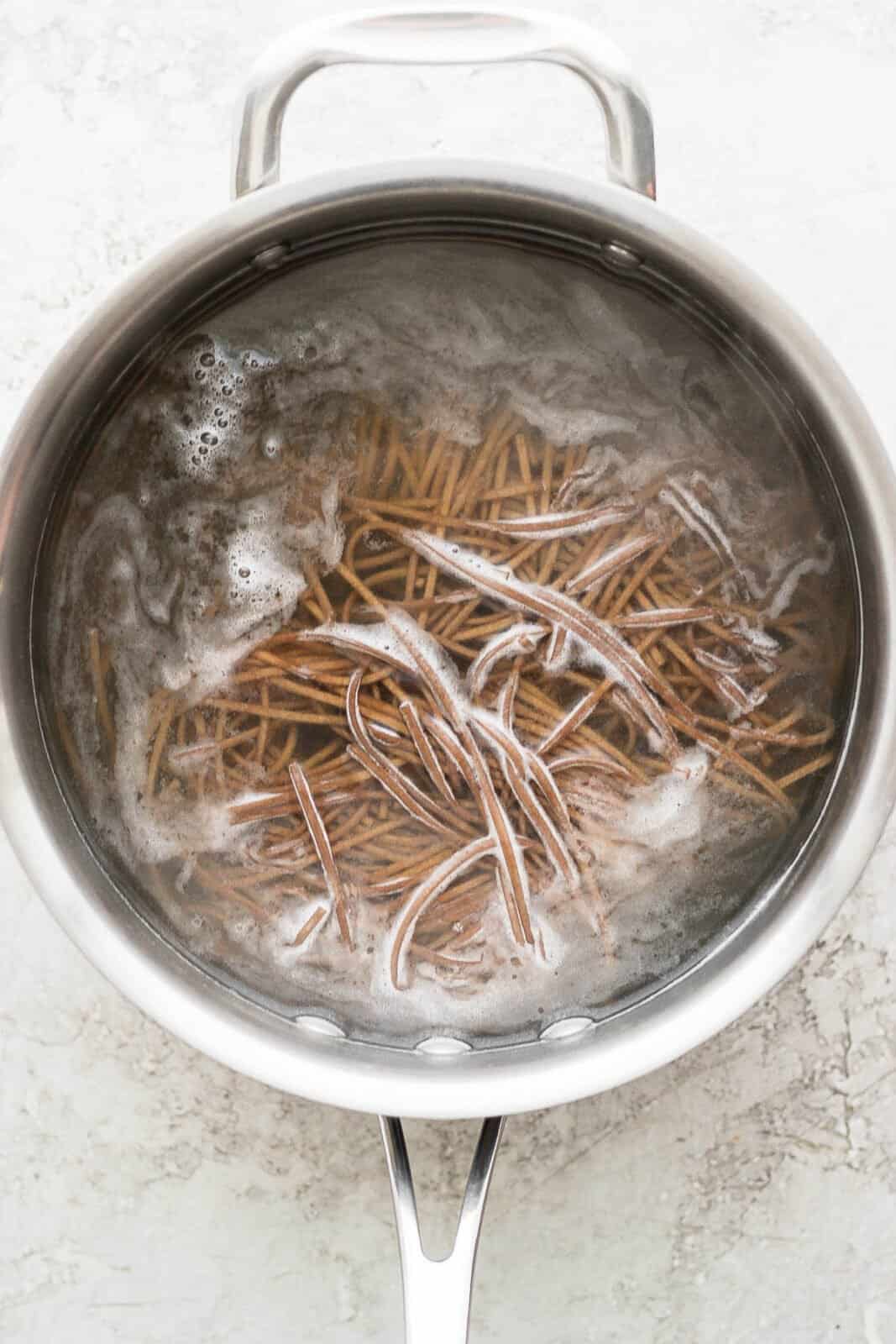 Soba noodles being cooked in a saucepan.