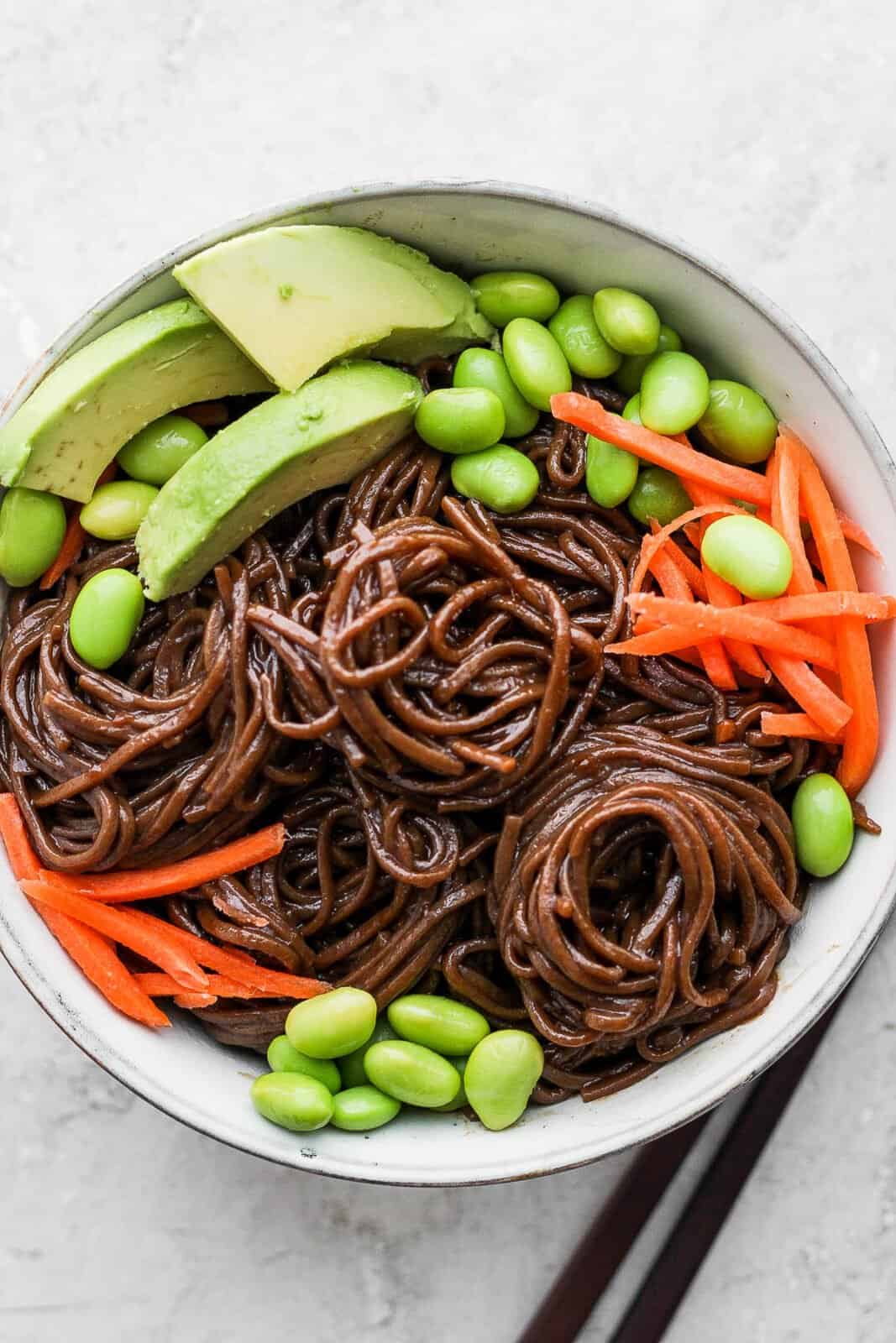 Bowl of soba noodles in sesame soy sauce with carrots, edamame and avocado. 