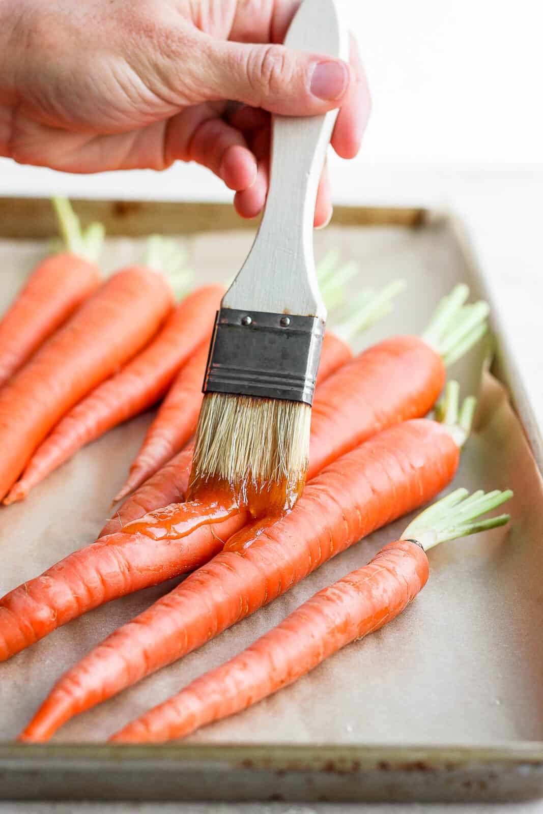 Someone brushing an olive oil and honey mixture on the carrots before roasting.