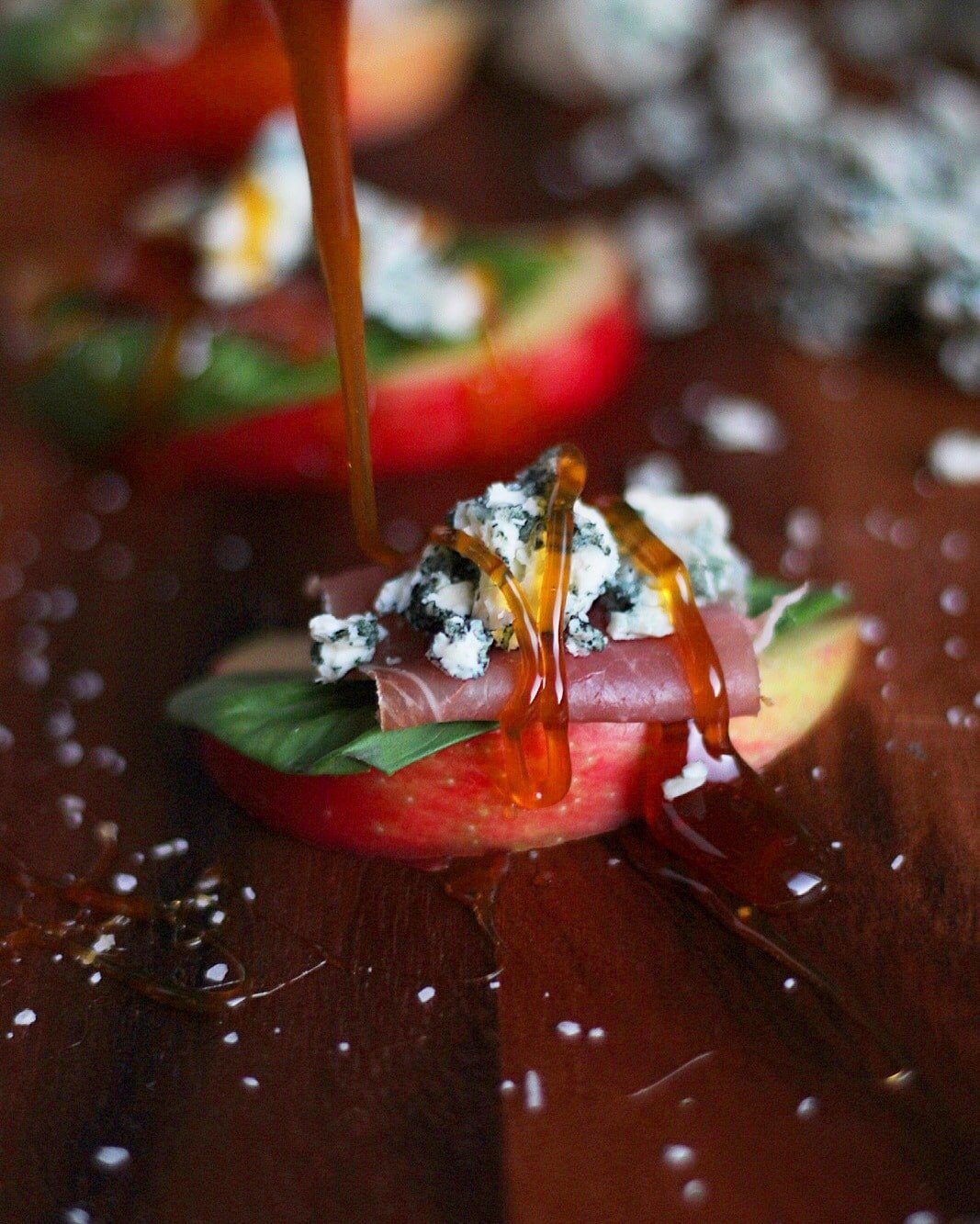 An apple slice topped with basil, prosciutto, blue cheese and honey. 